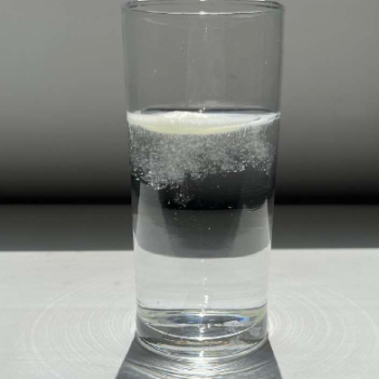 A clear glass filled with sparkling water, showcasing tiny bubbles rising to the surface against a soft gray background.
